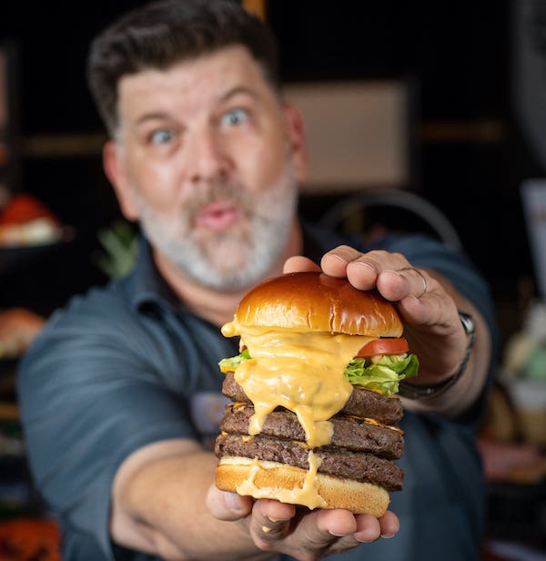 Man holding a four layered hamburger for Sizzle Restaurant Week