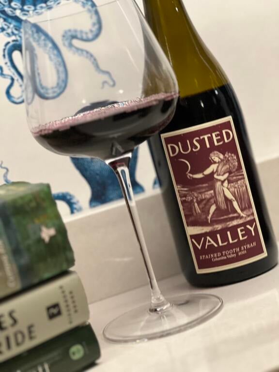 Bottle of Dusted Valley Stained Tooth Syrah on a white counter with a partially full wine glass next to it