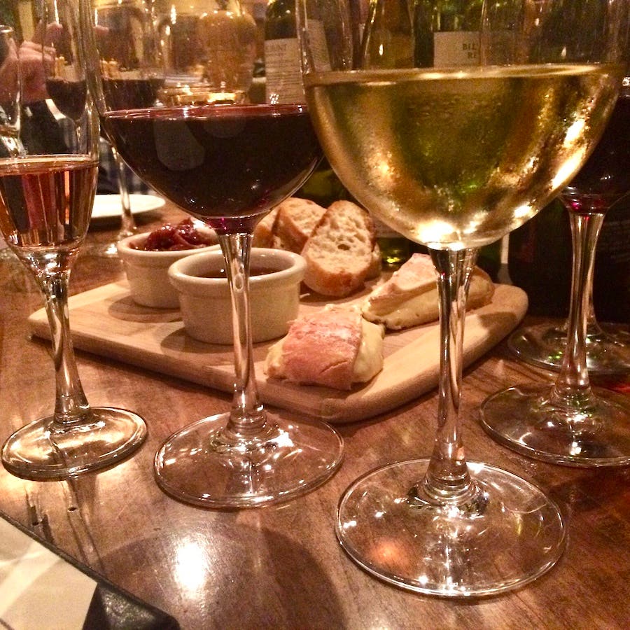 Table with numerous glasses full of wine, a cheese tray iwth bread in the middle for March wining and dining evens in SWFL