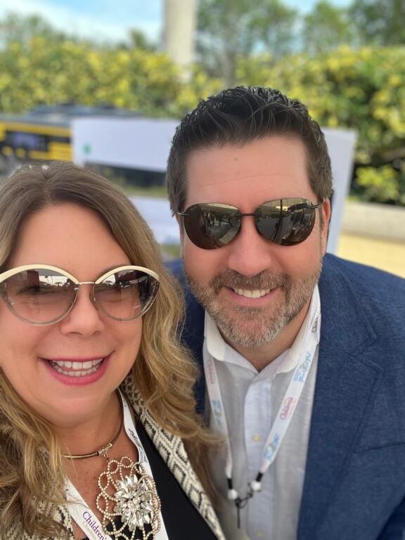 A girl and a man wearing sunglasses outside, smiling at the camera