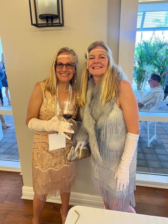 Two blond women in sparkling dresses, wearing long gloves and headbands in 1920's style of the SWFL wine and food fest