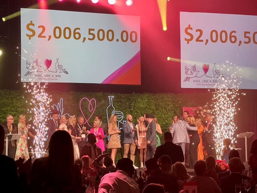 A stage lined with people and a neon sign reading $2,006,500.00 at a charity event for 15 SWFL Weekend events