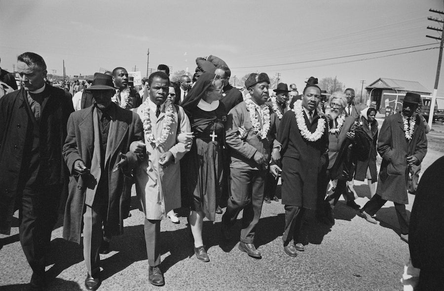 Black and white photo of Dr Martin Luther King Jr , arm in arm with a line of four men and women leading a group of people down the street, representing SWFL MLK Day parades and rallies