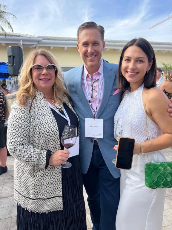 A man with his arms around two women holding wine glasses and smiling at the camera