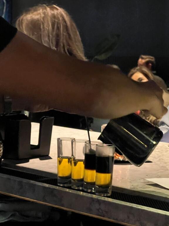 Four shot glasses lined up, a bar tender filling each with espresso