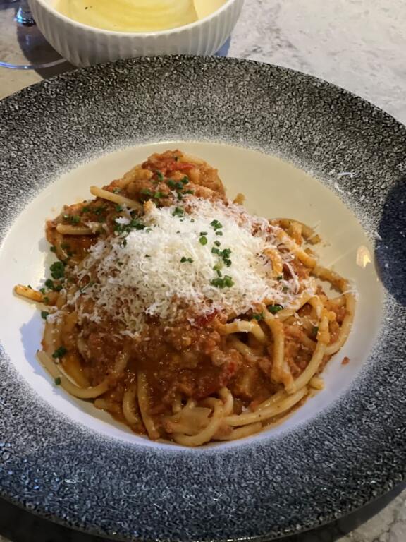 A plate of Bolognese, pasta with red meat sauce and topped with grated cheese 