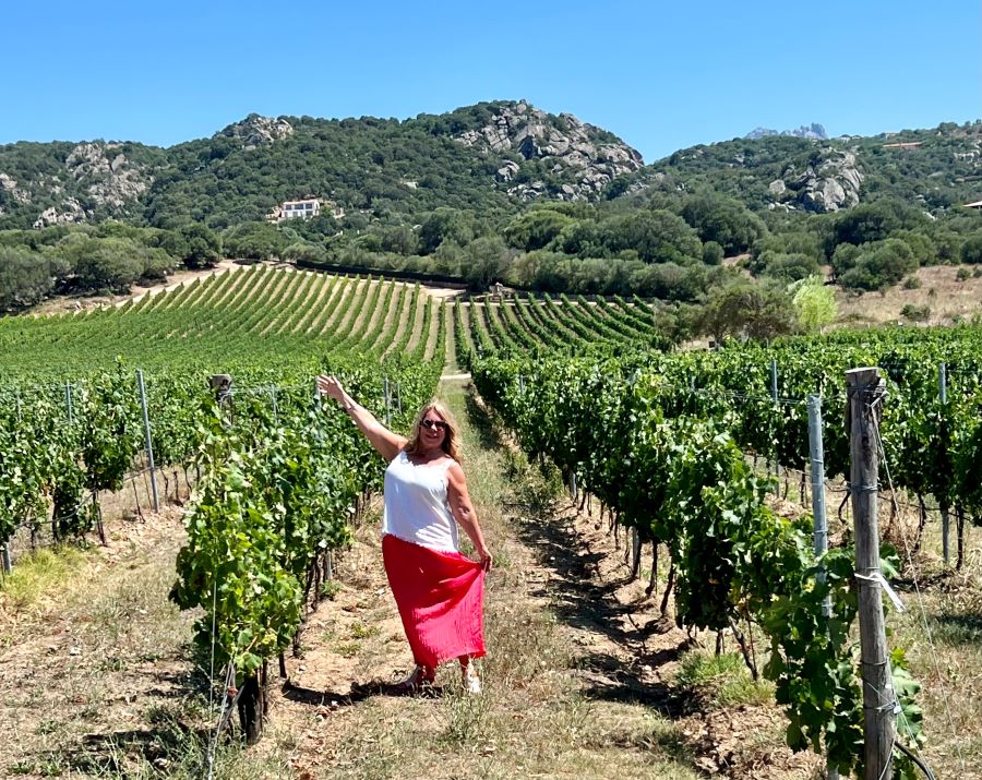 A girl in white shirt and long pink skirt in a vineyard with arms in the air for wines from Sardinia in Southwest Florida