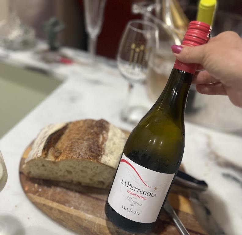 Bottle of La Pettegola Vermentino, Maremma on a wooden cutting board with a half loaf of bread, drink vermentino this summer