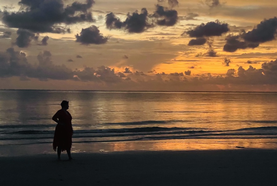 silohette of a woman on the beach with a brilliant red and orange sunset.