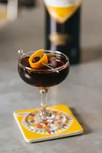 Dark cocktail in a coup glass with an orange twist for a garnish