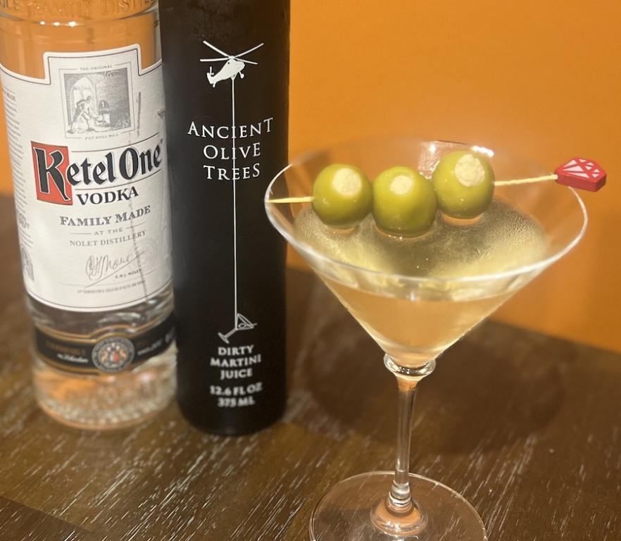 Bottle of Kettle Vodka, Ancient Olive Trees and a martini glass with a dirty martini and olive To Get Dirty At Cocktail Time 